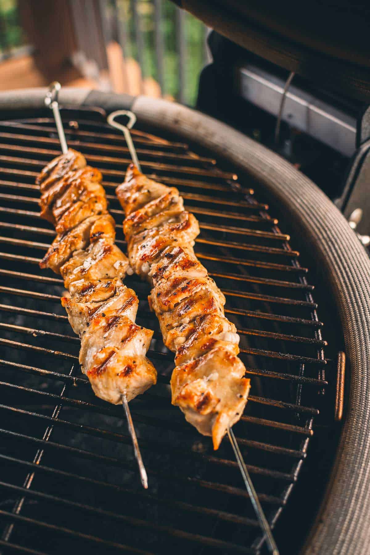 Two skewers of grilled meat are on a barbecue grill.