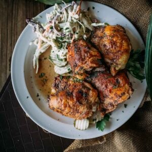 A plate with four pieces of grilled chicken thighs and a serving of coleslaw.