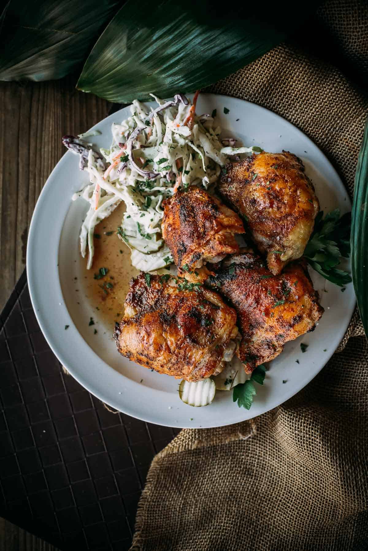 A plate with four pieces of grilled chicken thighs and a serving of coleslaw.