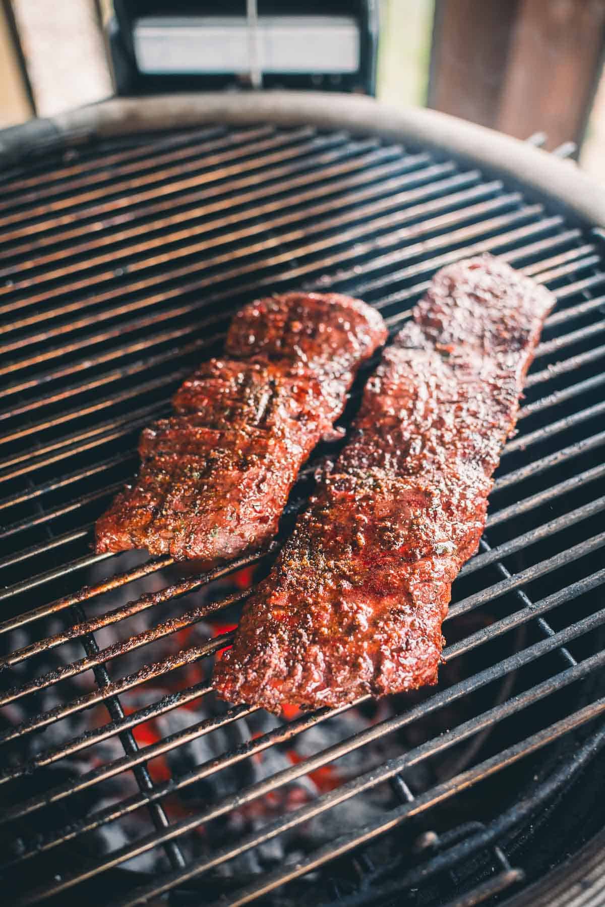 Two slabs of seasoned meat cooking on a grill.