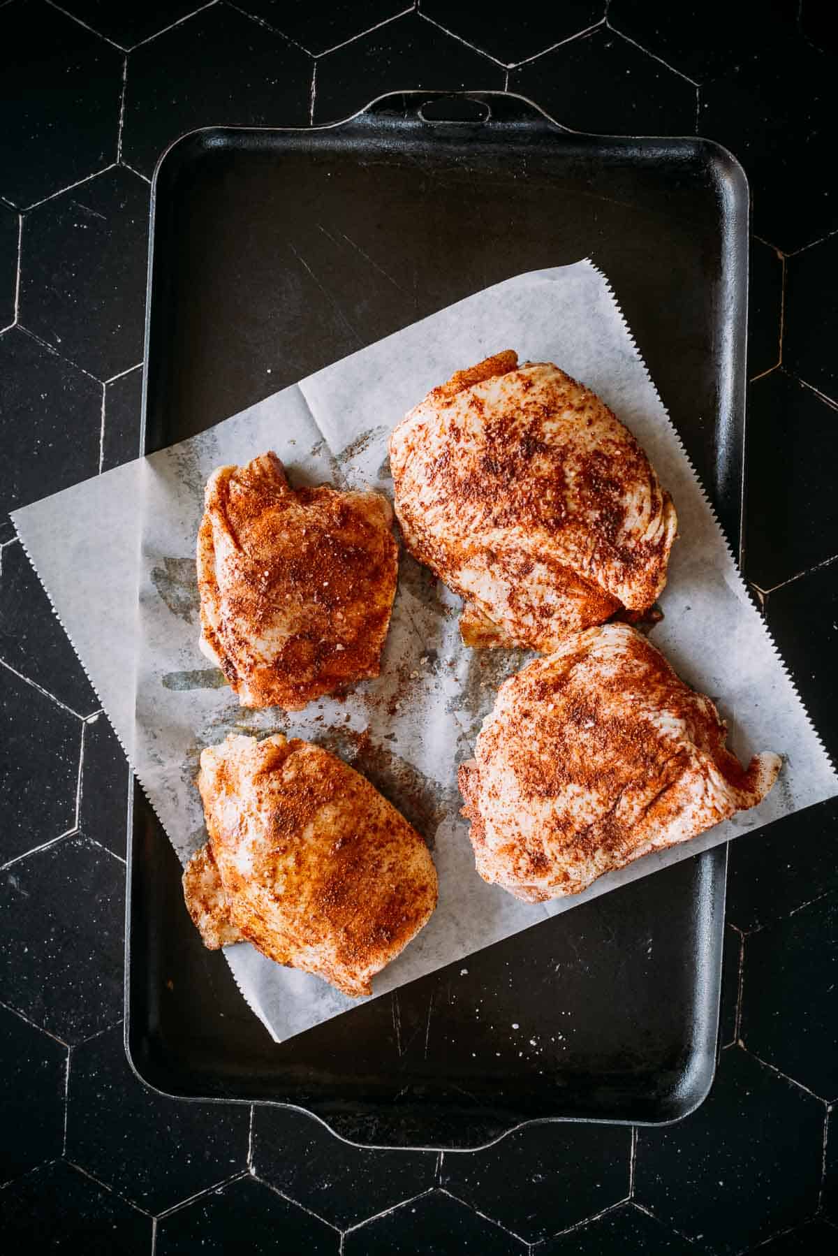 Four seasoned pieces of raw chicken on a parchment paper-lined baking sheet, ready for cooking.