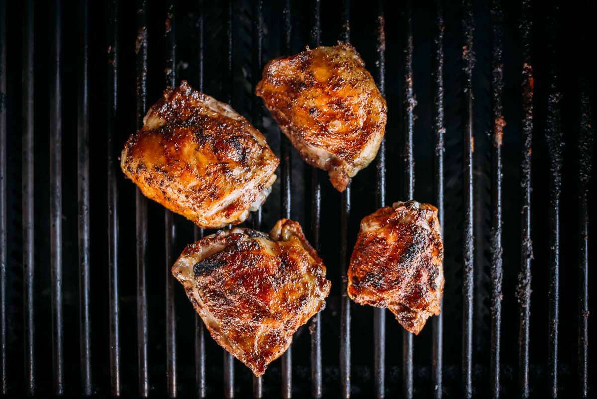 Four pieces of seasoned, grilled chicken sit on a black grill grate with visible char marks.