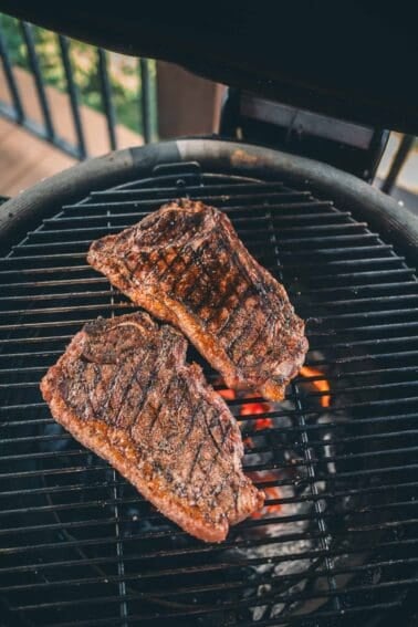 Two seasoned steaks are cooking on a round grill with visible grill marks.