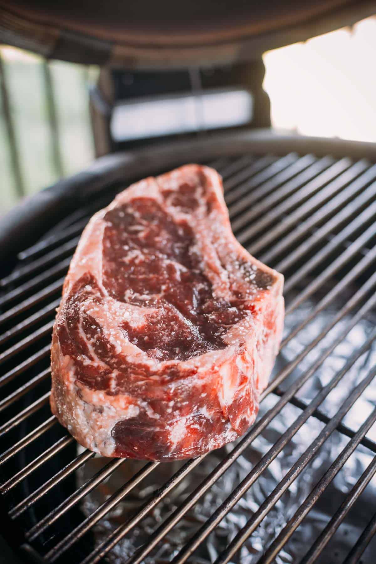 A thick raw steak seasoned with salt placed on a grill grate.