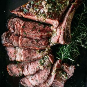 Slices of smoked steak with herbs and seasoning on a black surface, garnished with a sprig of rosemary.