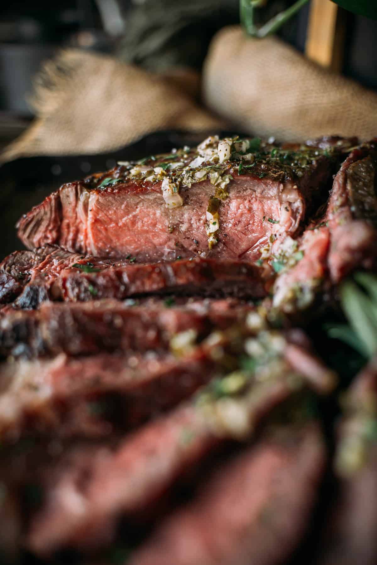 Close-up of sliced medium-rare ribeye steak garnished with chopped herbs and garlic.
