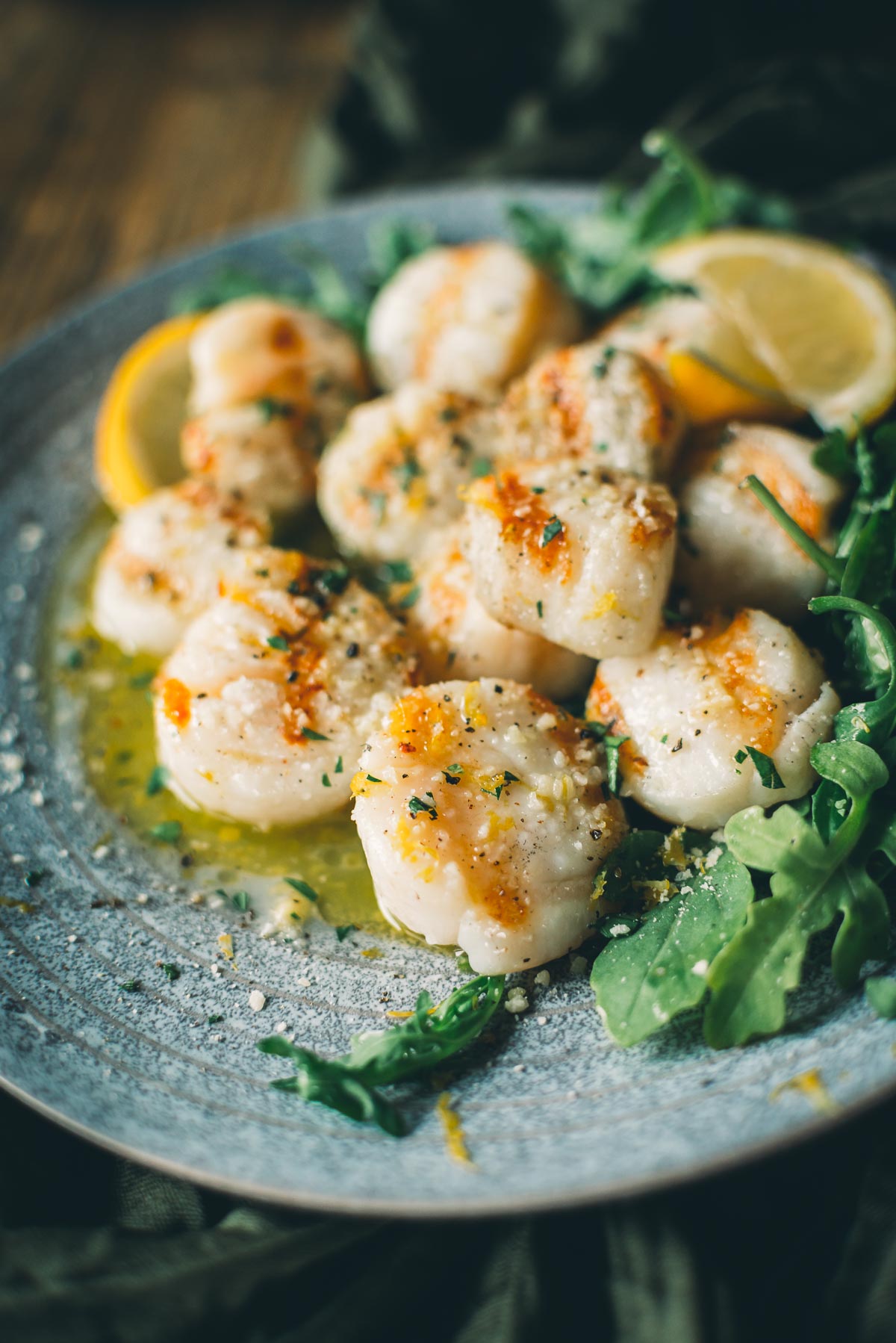 A plate of grilled scallops garnished with herbs and arugula, served with lemon wedges on a textured blue plate.