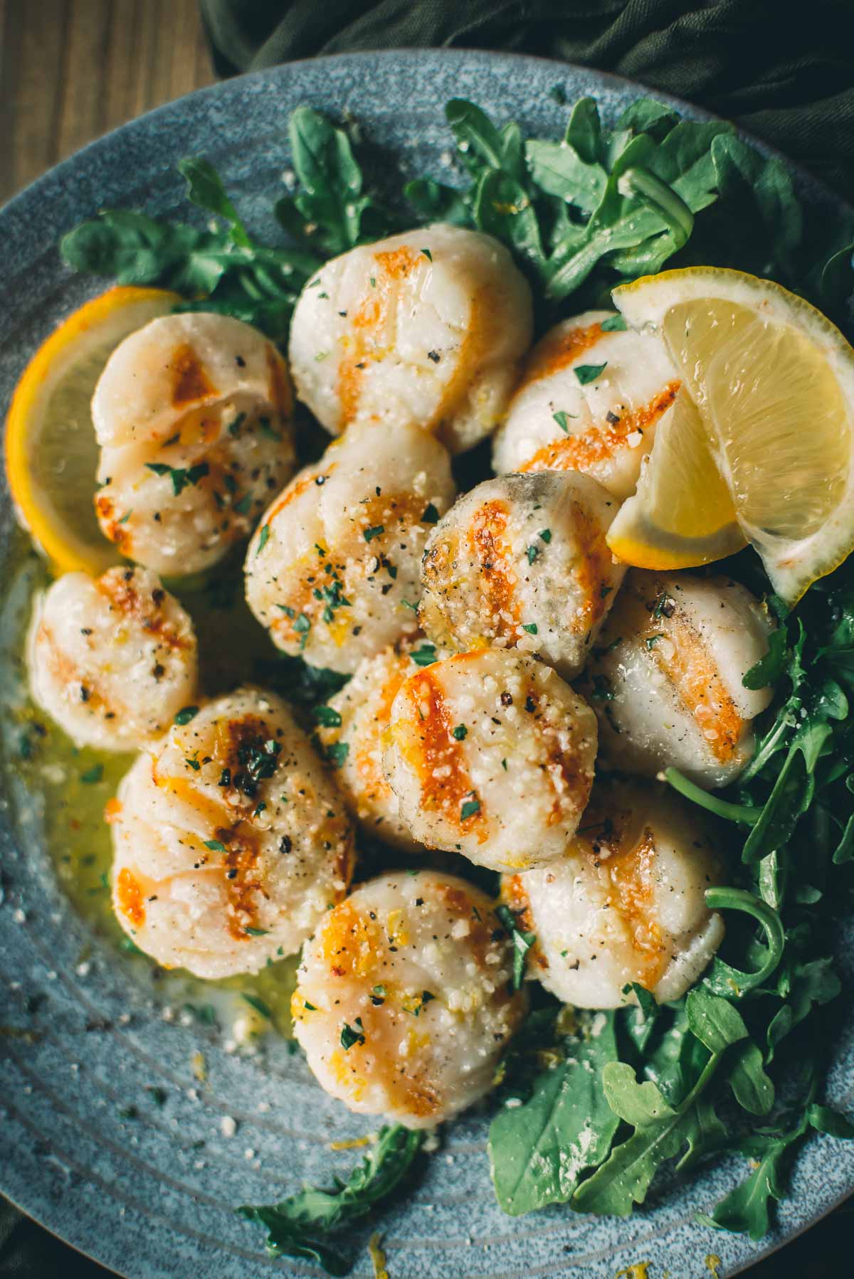 A plate of grilled scallops garnished with lemon wedges and served on a bed of leafy greens.