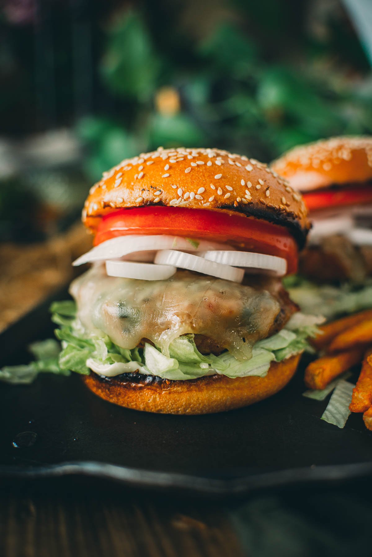 A close-up of a ground pork burger with lettuce, sliced onions, tomato, and a sesame seed bun.