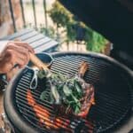 A person grills a large steak with fresh herb basting brush on a barbecue grill.