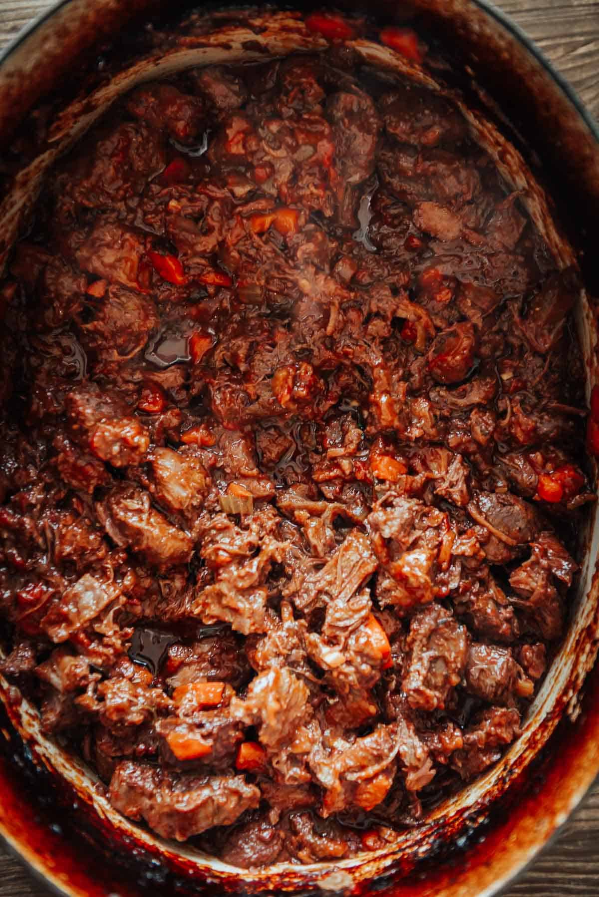 A close-up view of a pot filled with cooked, shredded meat and vegetables in a rich, dark sauce.