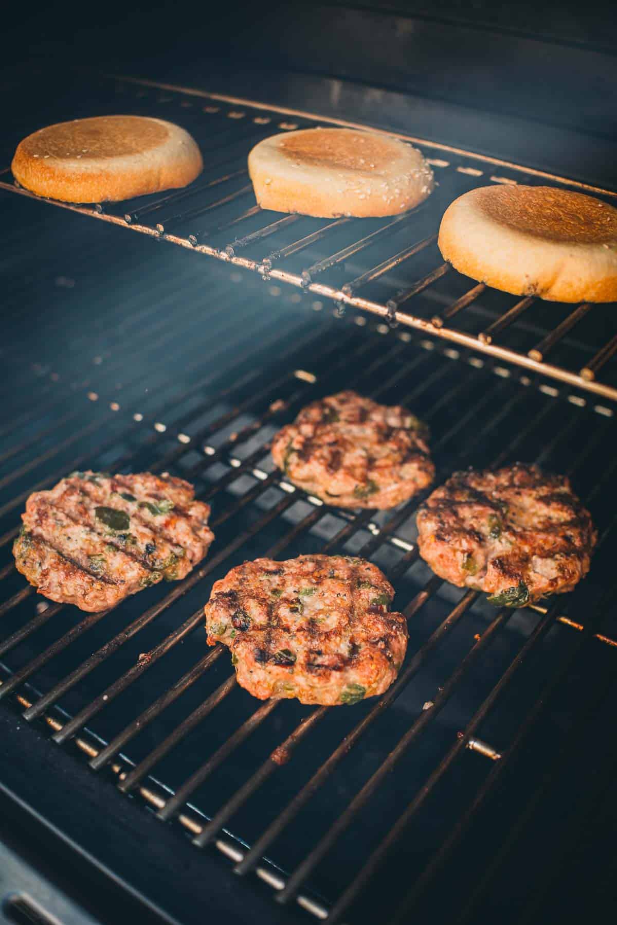 Four beef patties and three burger buns are being grilled on a barbecue.