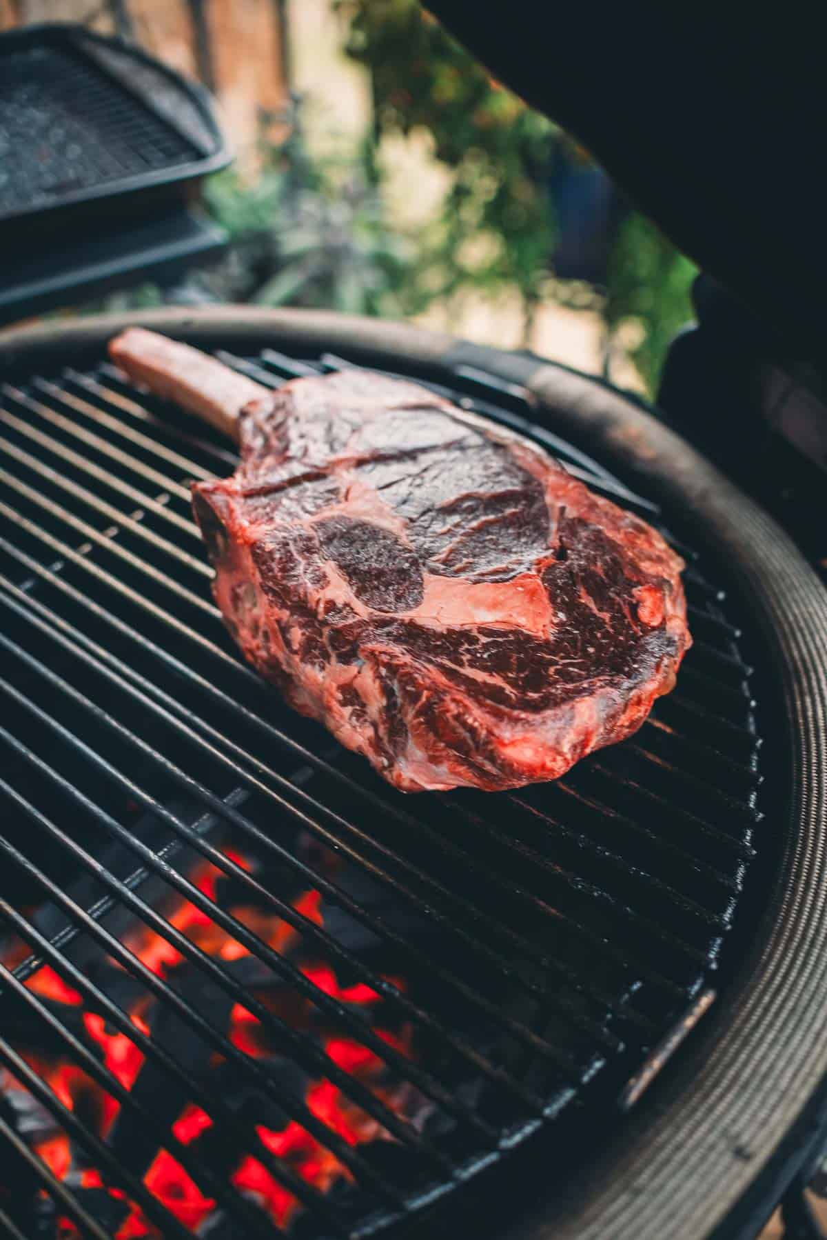 A large raw steak is placed on a grill with glowing red coals beneath it.