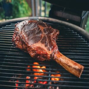 A cowboy steak is being grilled over an open flame on a barbecue grill.