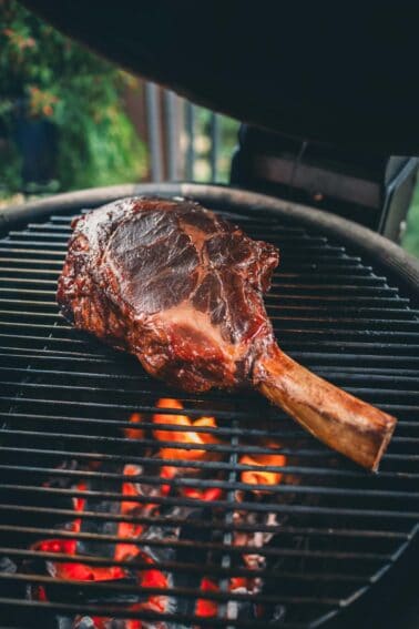 A cowboy steak is being grilled over an open flame on a barbecue grill.