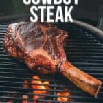 A grilled cowboy steak cooking on a barbecue with flames beneath. Text reads "How to make grilled cowboy steak." The bottom of the image directs viewers to GirlCarnivore.com for the full recipe.