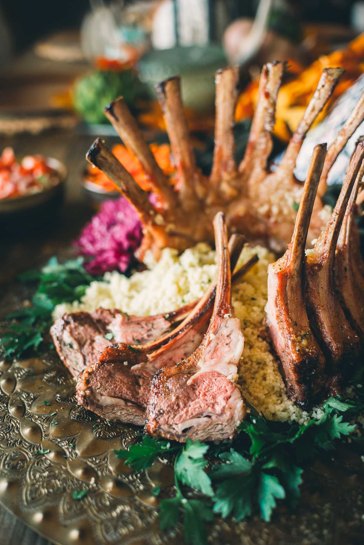 A cooked lamb crown rosat served on a metal plate with couscous and garnished with fresh herbs.