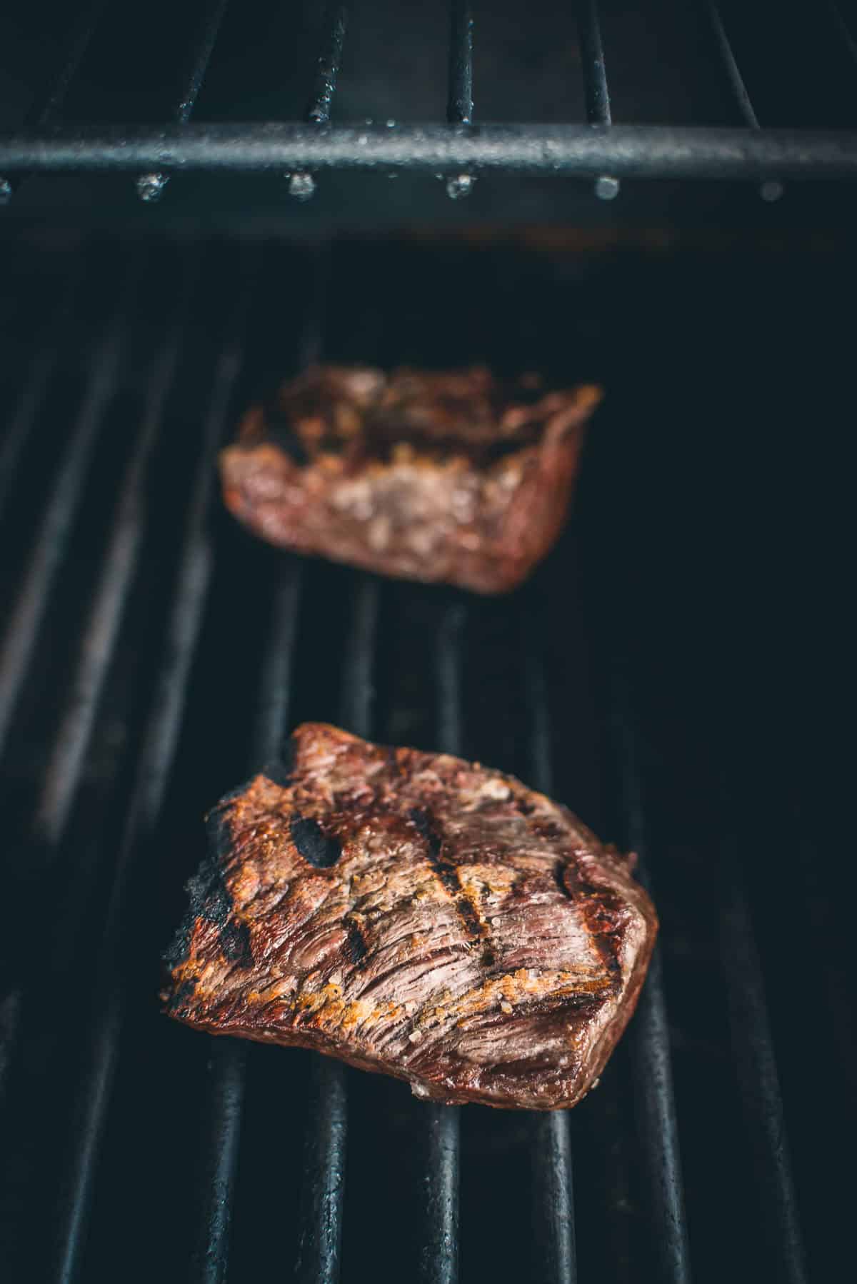 Two pieces of grilled steak on a black grill grate, with visible grill marks.