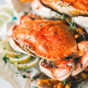 Close-up of cooked crabs served on a parchment paper bed with lemon slices and garnished with herbs.