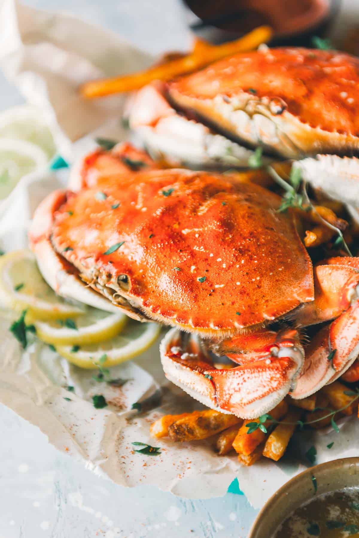 Close-up of cooked crabs served on a parchment paper bed with lemon slices and garnished with herbs.