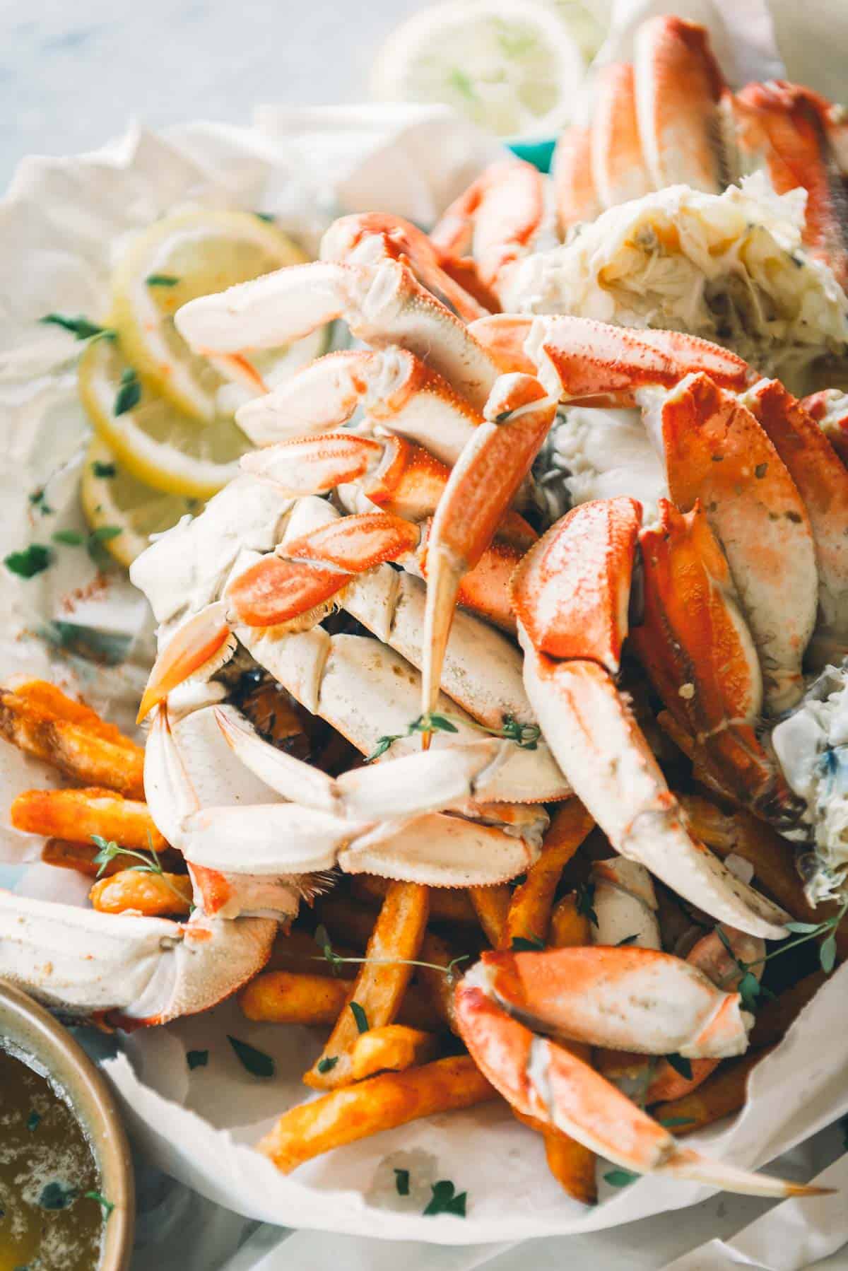 A plate filled with cooked crab legs and seasoned fries, garnished with lemon slices and chopped herbs.