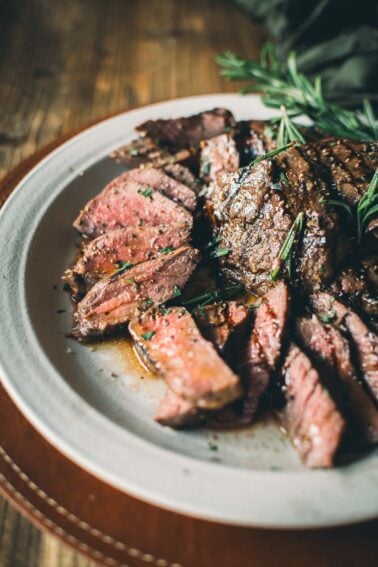 A plate of sliced medium-rare elk steaks garnished with rosemary, served on a rustic wooden table.