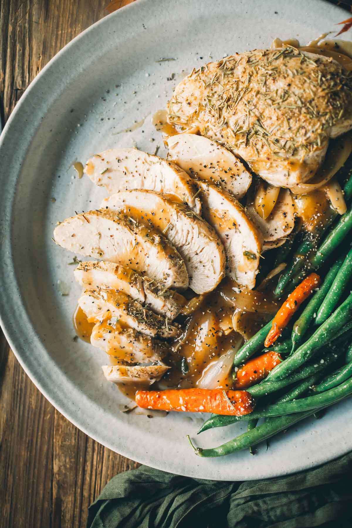 A plate of sliced roast turkey tenderloin with gravy, served with green beans and carrots, on a wooden table.