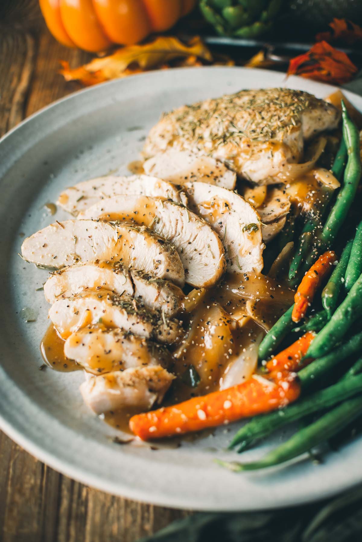 A plate of sliced turkey tenderloin covered in gravy, served with green beans and baby carrots.