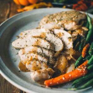 A plate with sliced roasted turkey, green beans, and carrots is served and garnished with gravy. A small pumpkin is in the background.