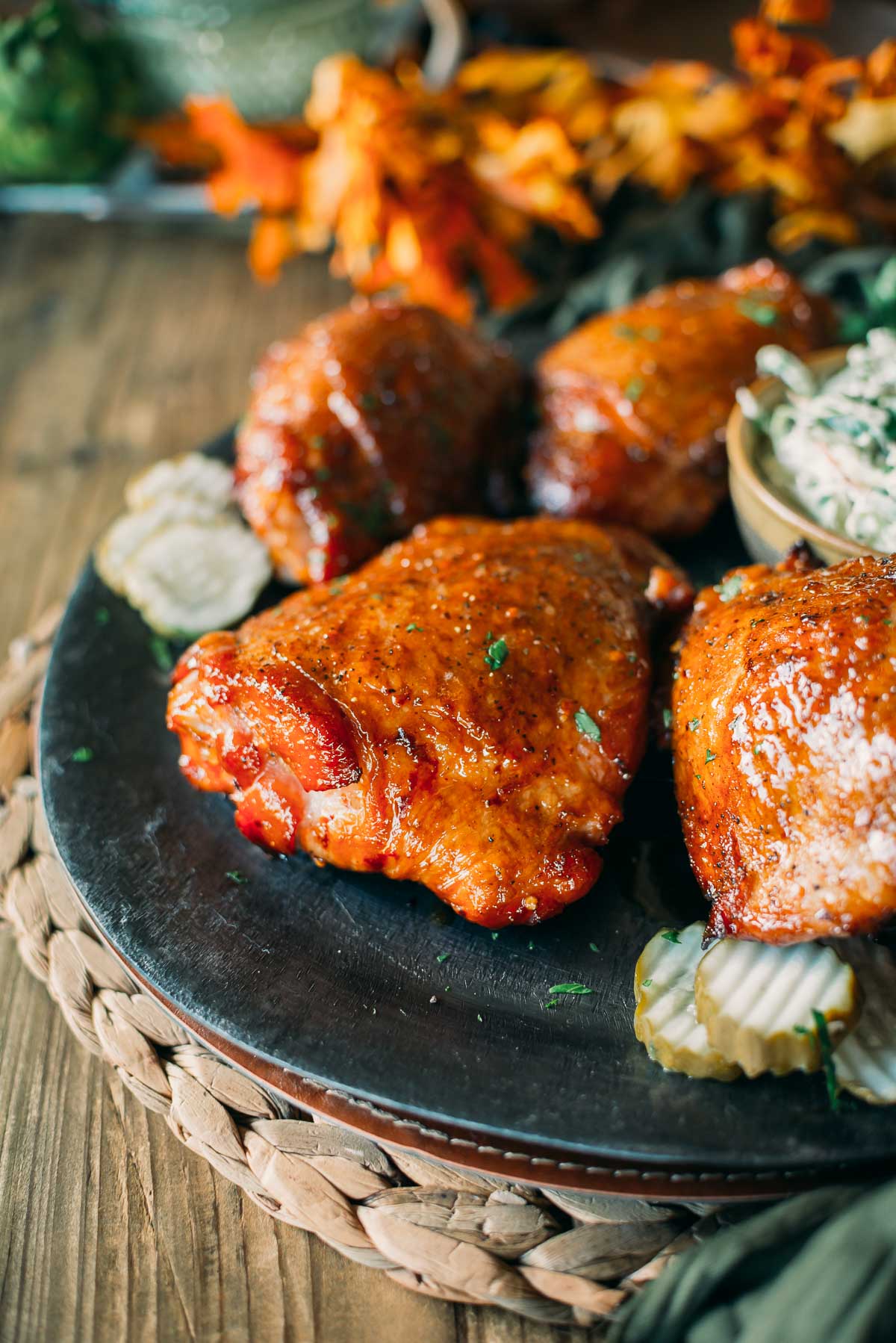 Smoked turkey thighs on a plate garnished with herbs, accompanied by pickles and coleslaw, placed on a woven mat.