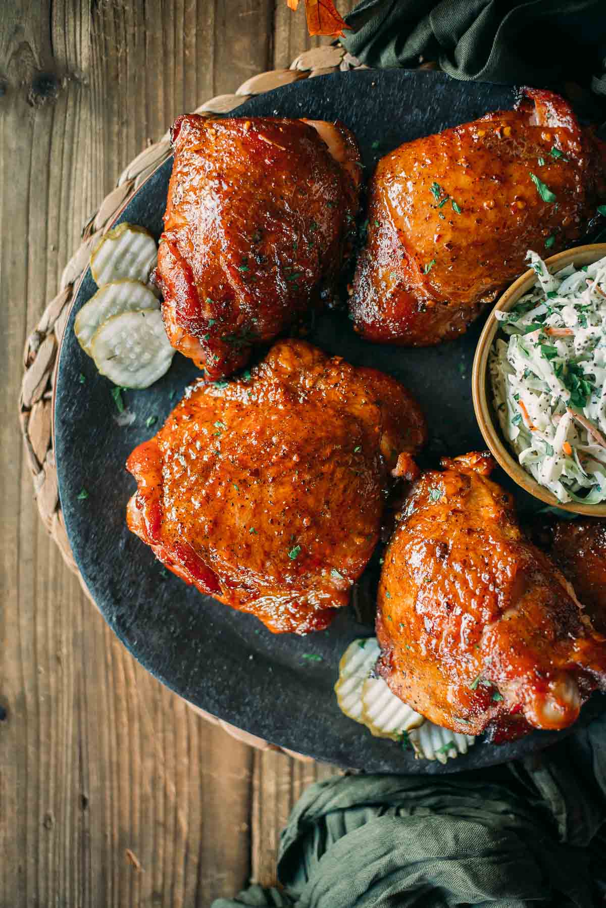 A plate of smoked turkey thighs, garnished with herbs, pickles on the side, and a small bowl of coleslaw.