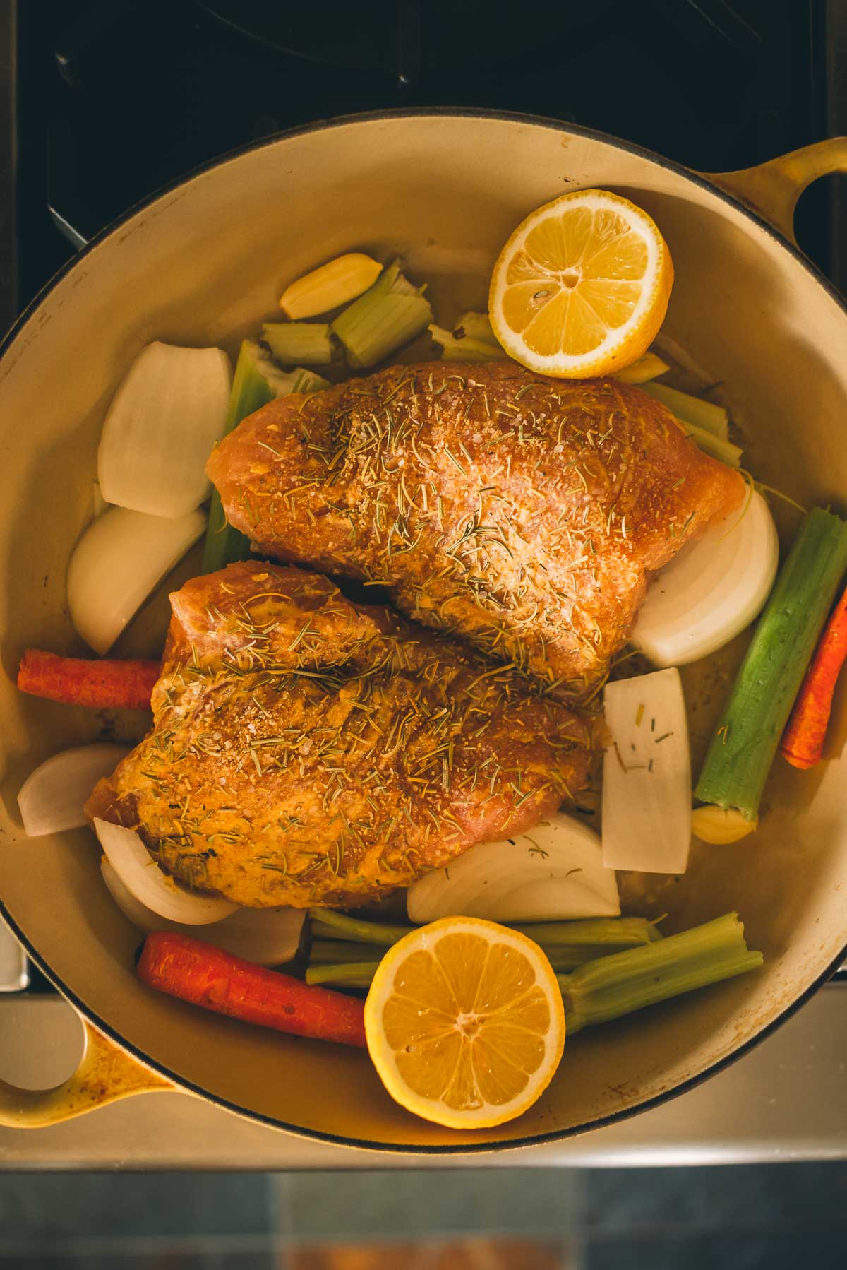 A roasting pan filled with seasoned raw turkey tenderloin pieces, lemon halves, onions, carrots, celery, and garlic cloves, ready to be cooked.