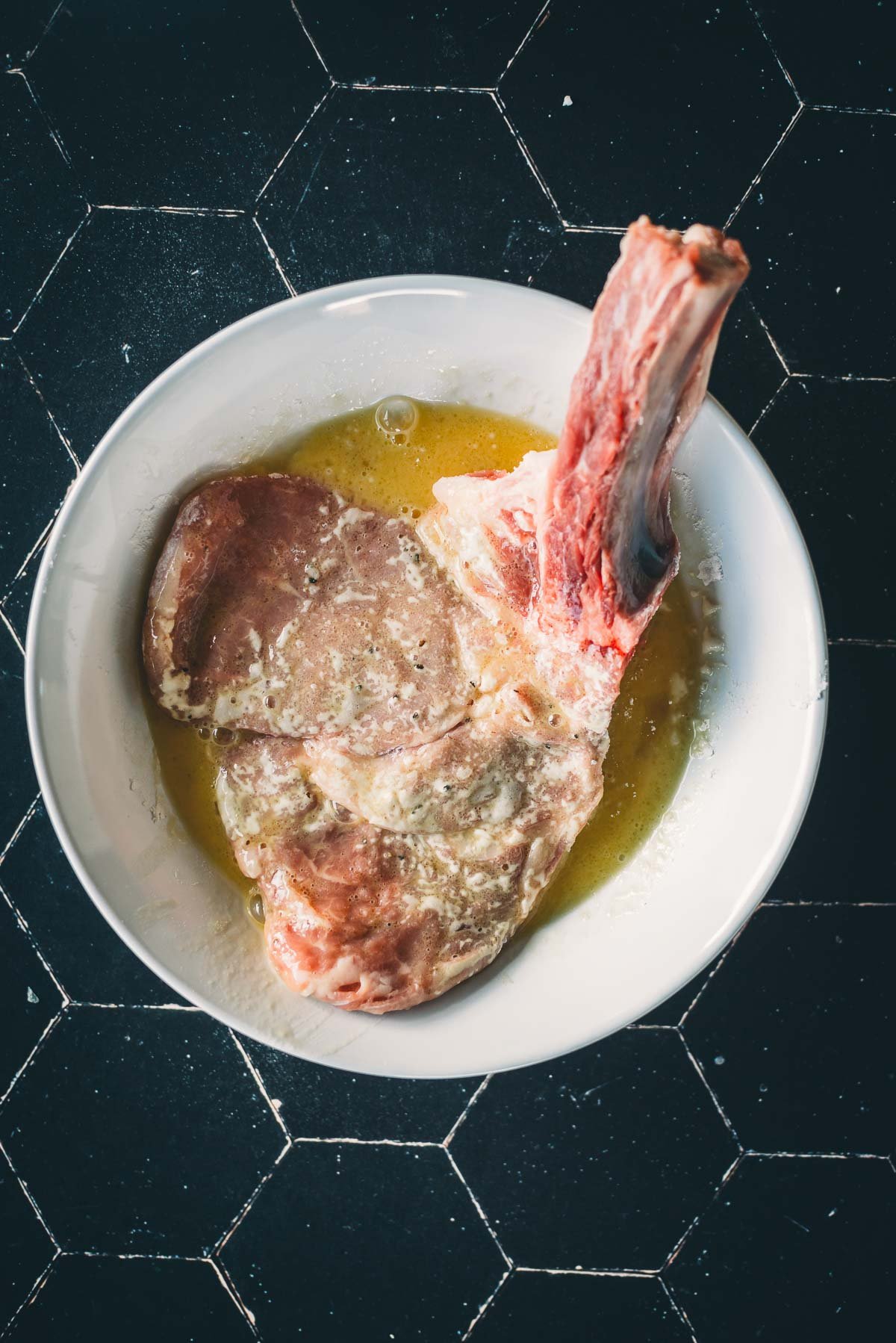 A veal chop dipped in an egg wash as part of the breading process. 