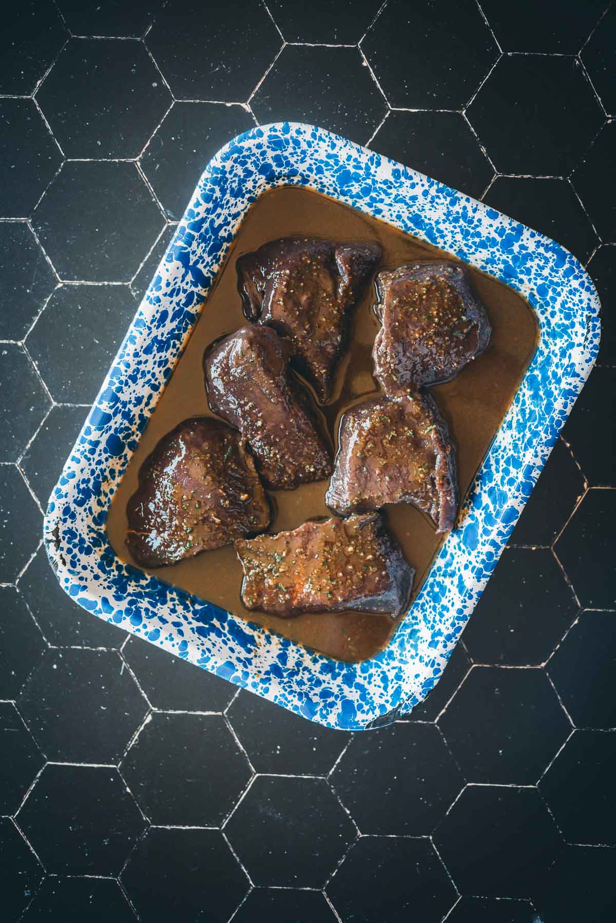 A blue-speckled tray contains six pieces of marinated elk in a balsamic marinade.