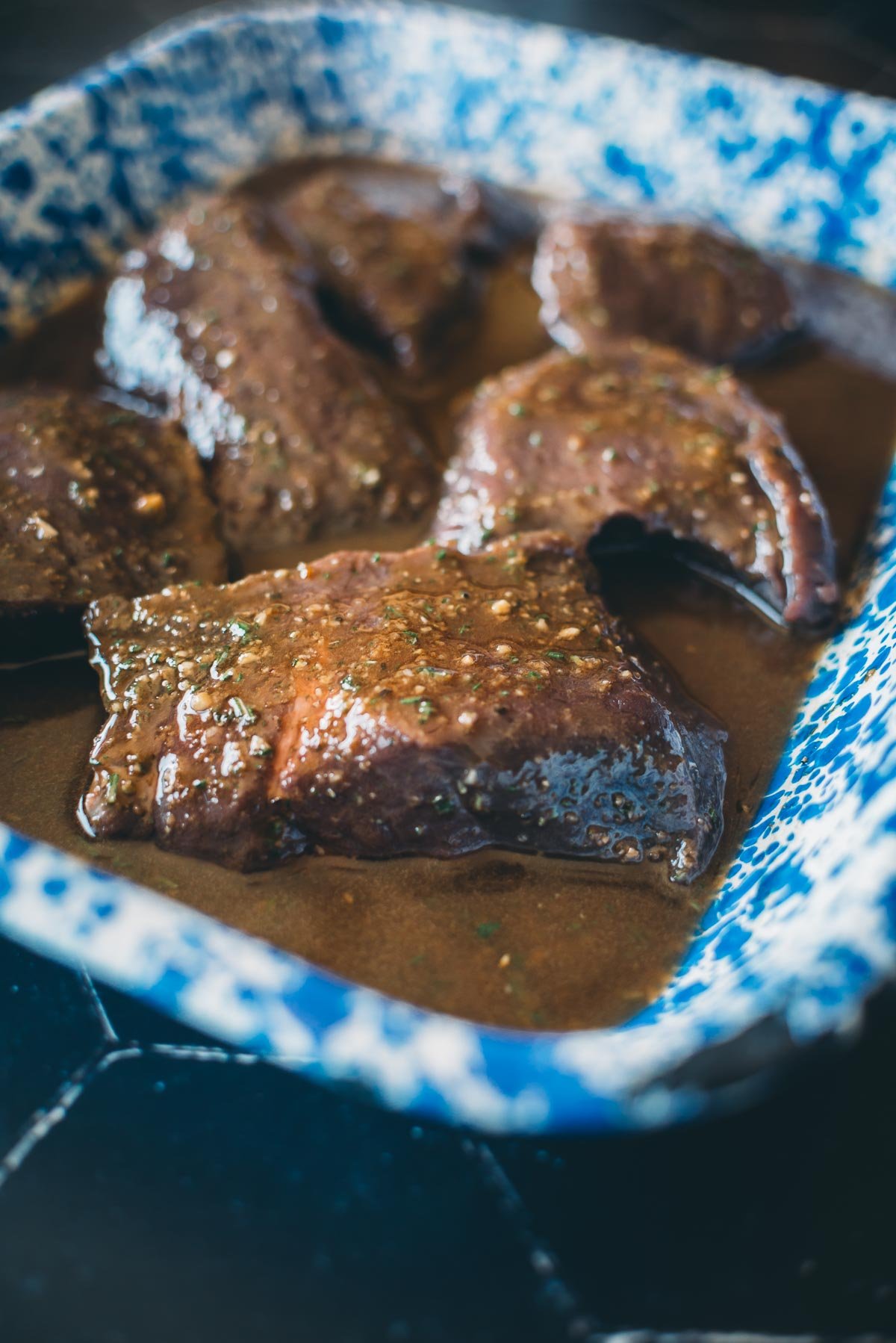 Slices of meat in a thick, brown sauce served in a blue and white speckled dish.