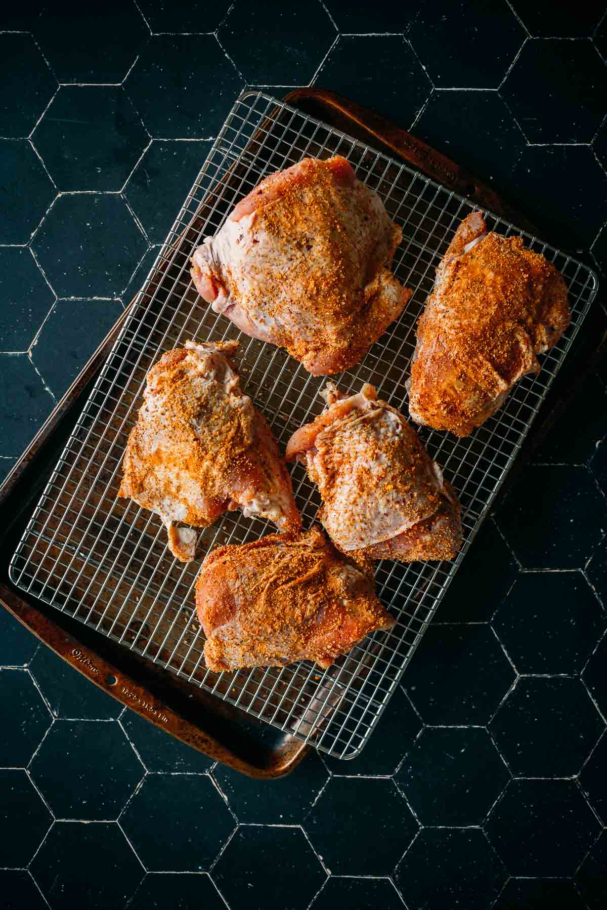 Five seasoned turkey thighs arranged on a wire rack placed over a baking sheet, ready for cooking.