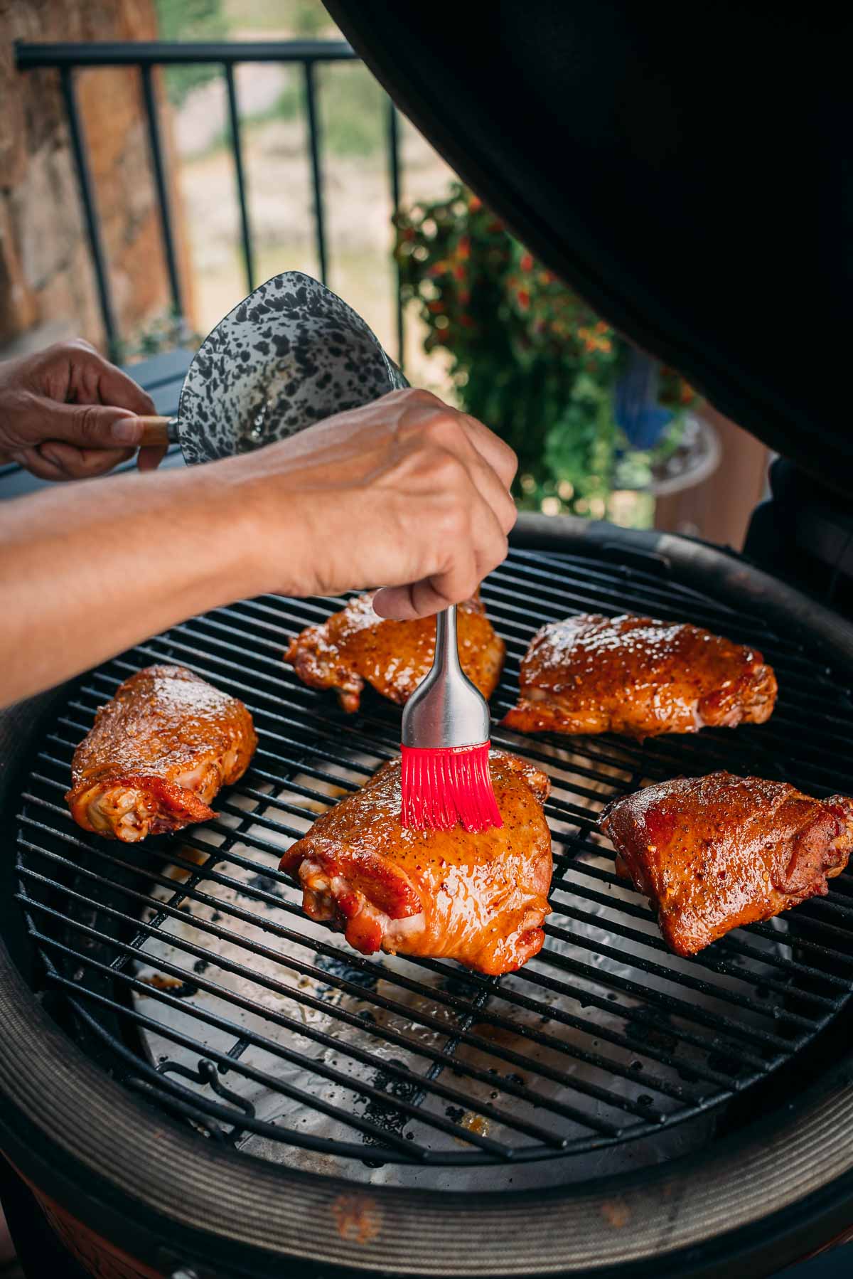 A person brushes glaze on pieces of turkey cooking on a grill.