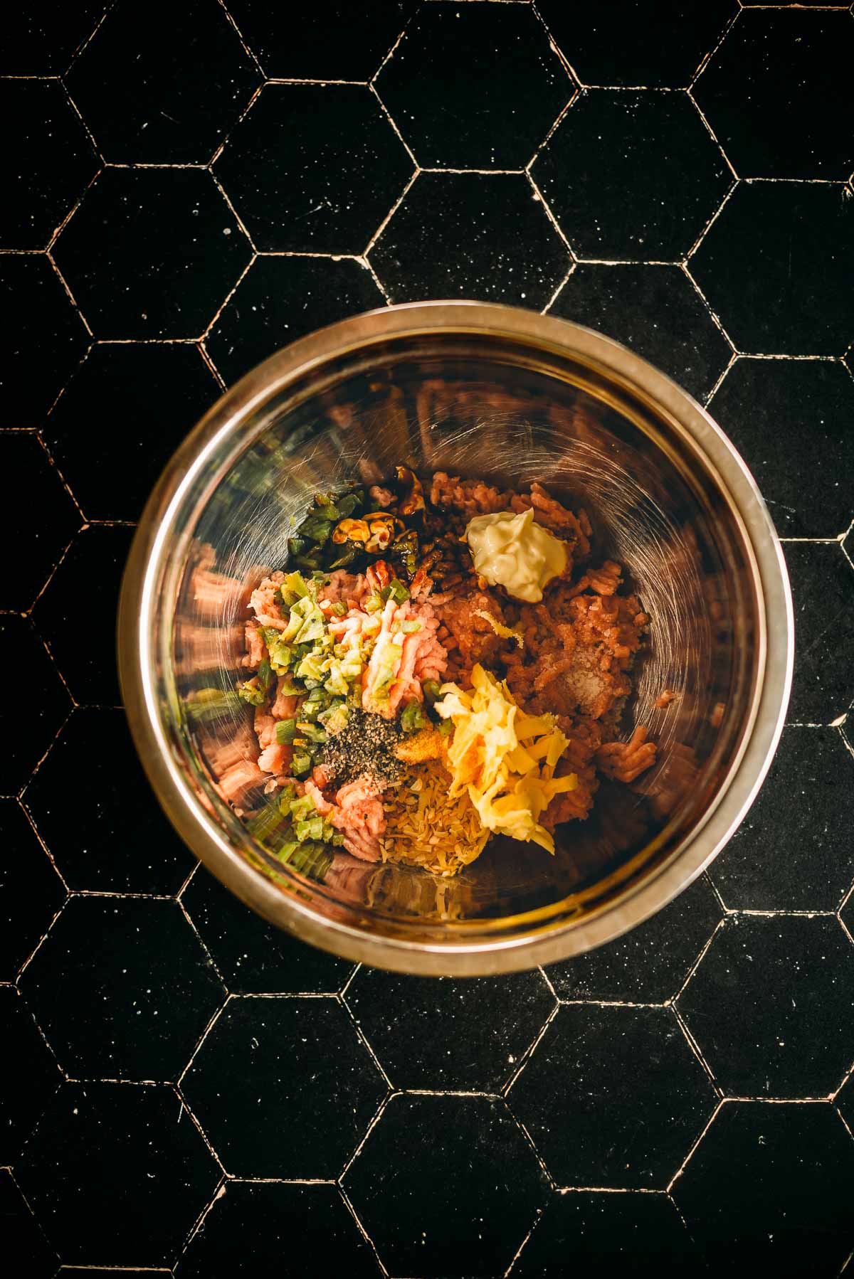 Top view of a mixing bowl containing ground turkey mixture, chopped vegetables, grated cheese, and seasonings.