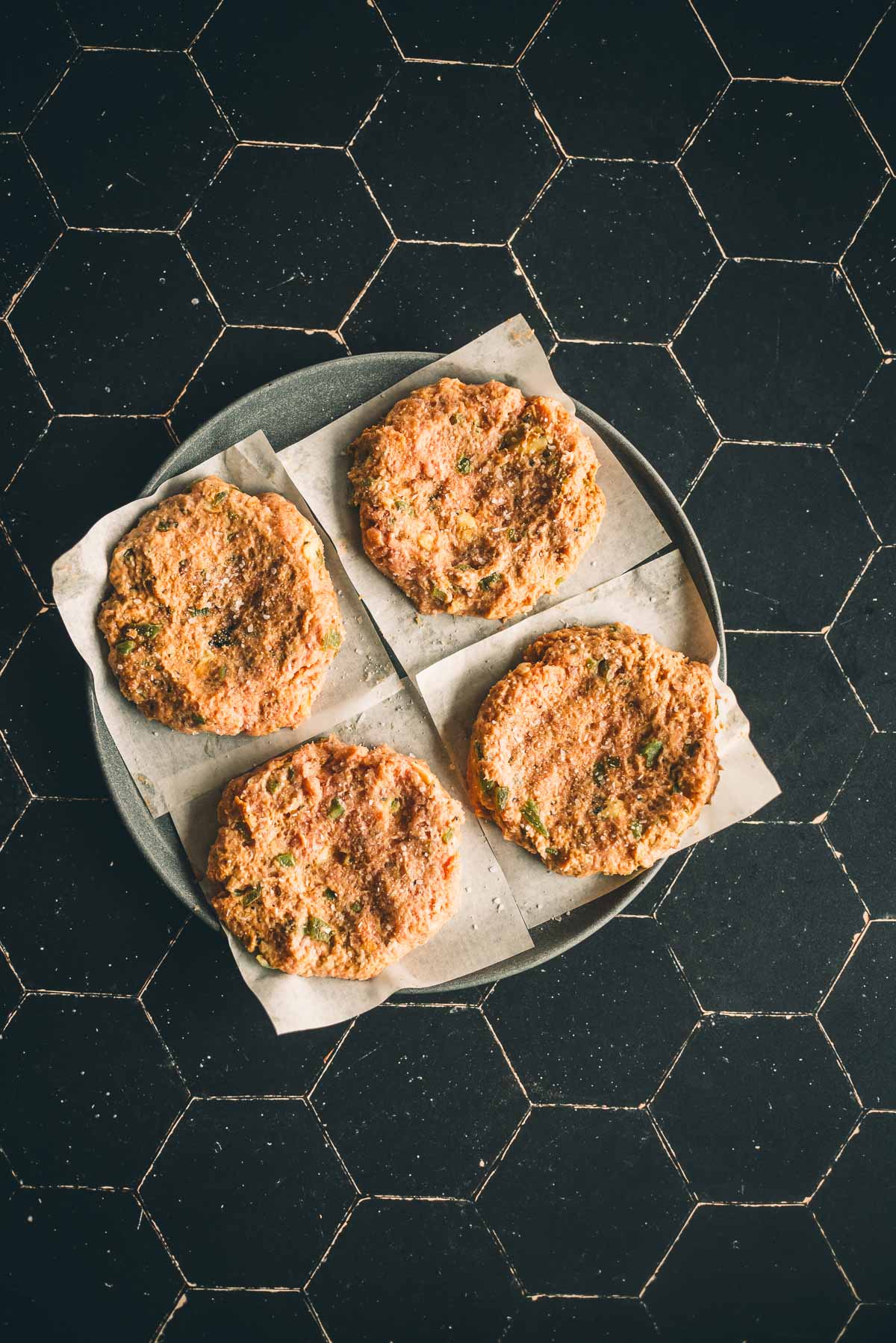 Four turkey burger patties on squares of parchment paper, arranged on a round plate.