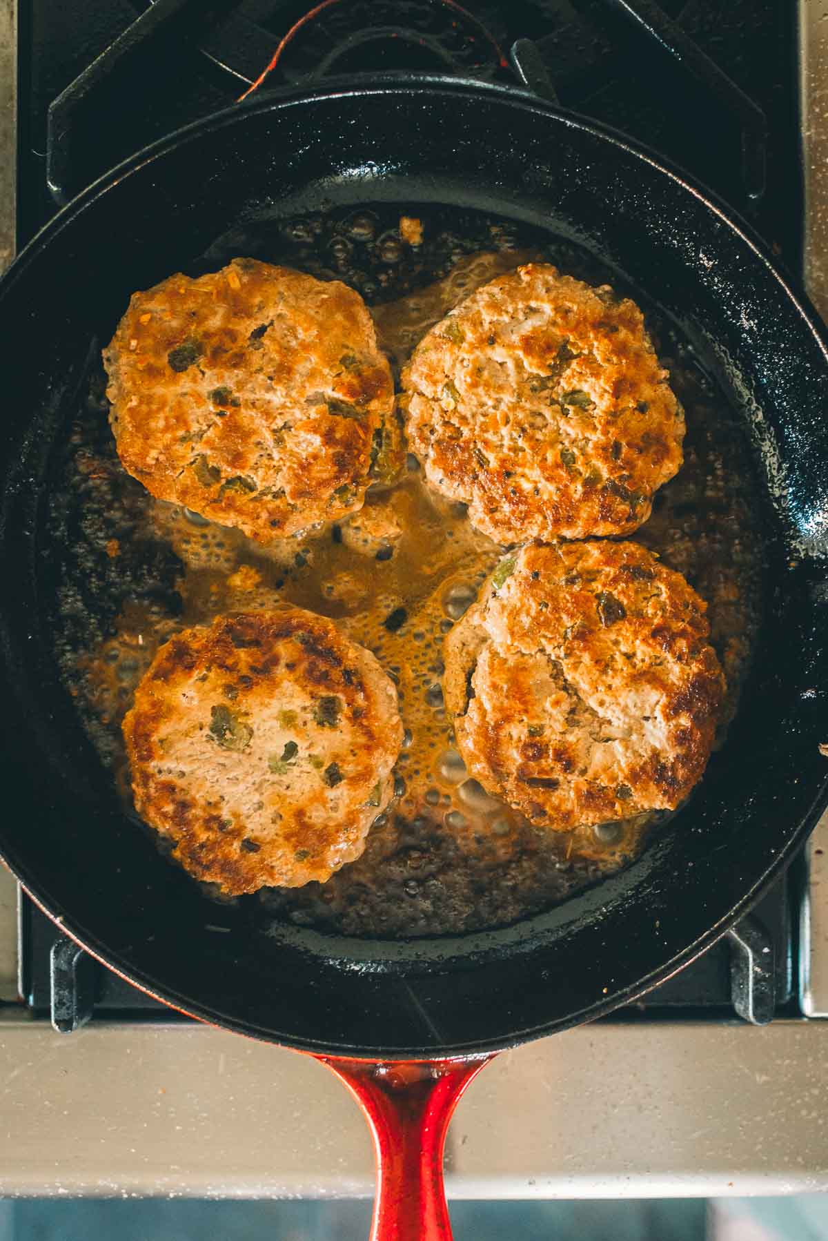 Four browned patties cooking in a skillet on a stovetop.