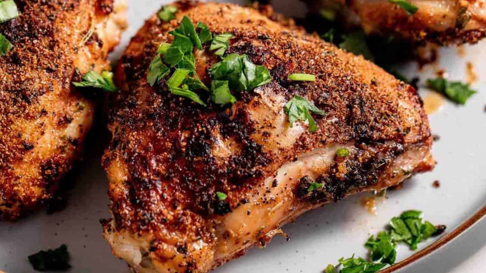 Close-up of seasoned and cooked chicken pieces garnished with fresh herbs on a plate.