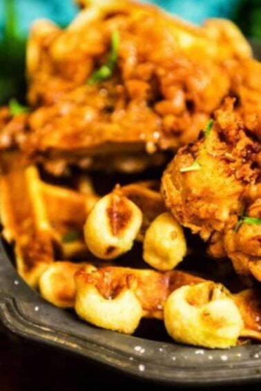 A plate of fried chicken on waffles, garnished with herbs.