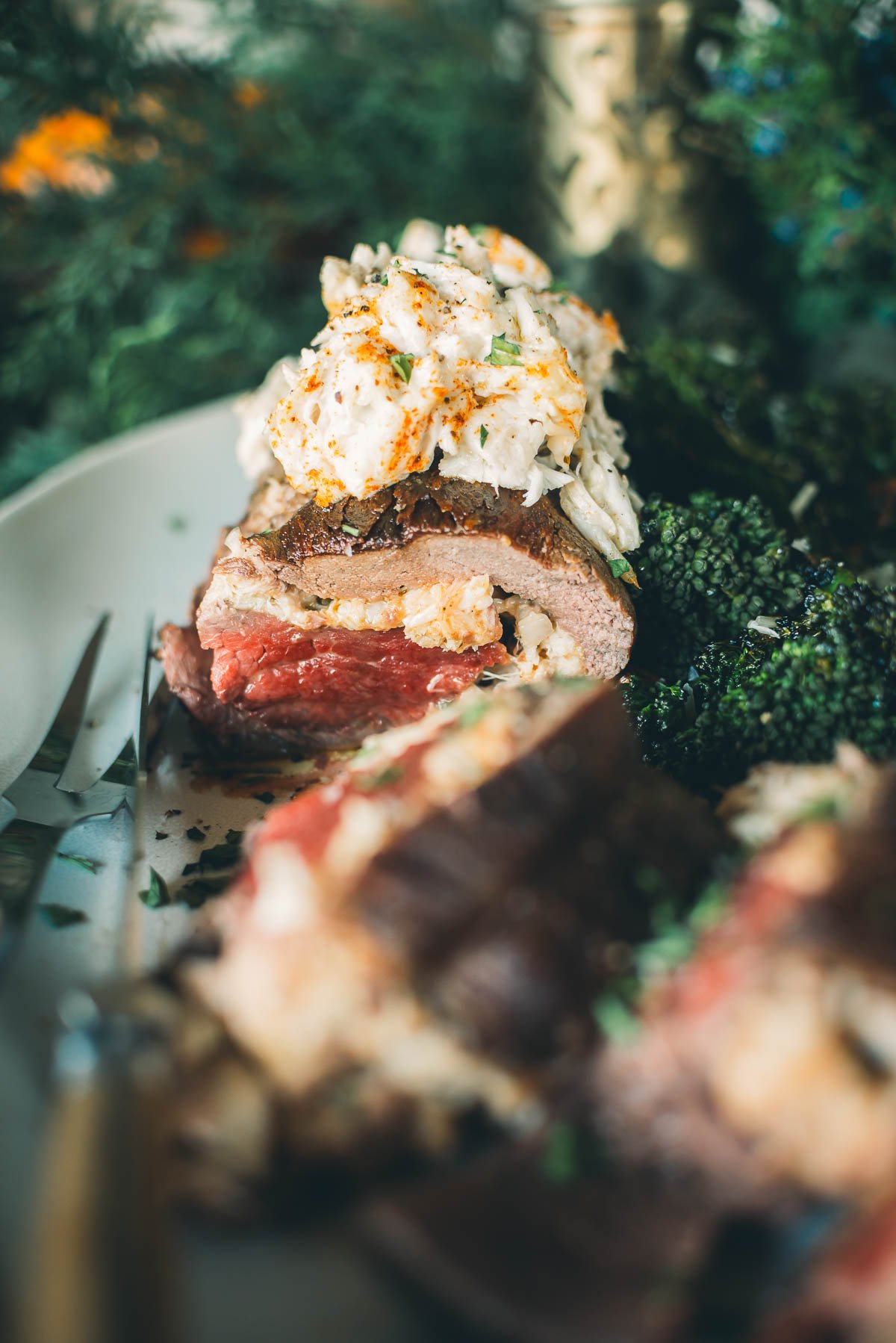 A stuffed beef tenderloin with creamy crab meat sits on a plate with a side of broccoli.