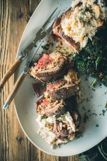 Sliced beef tenderloin stuffed with crab filling, served with baby broccoli on an oval white plate with a wooden-handled fork.