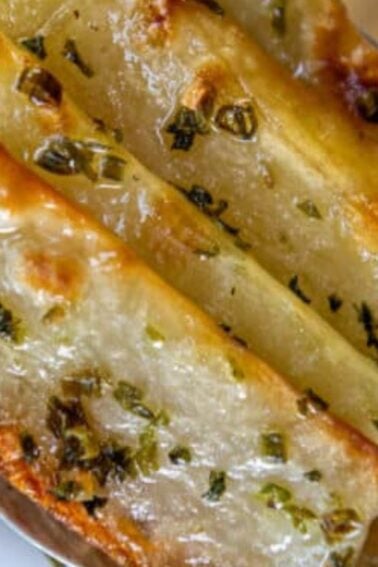 Close-up of three golden, herb-topped baked potato wedges arranged on a metal spoonโperfect for your list of Thanksgiving recipe ideas.