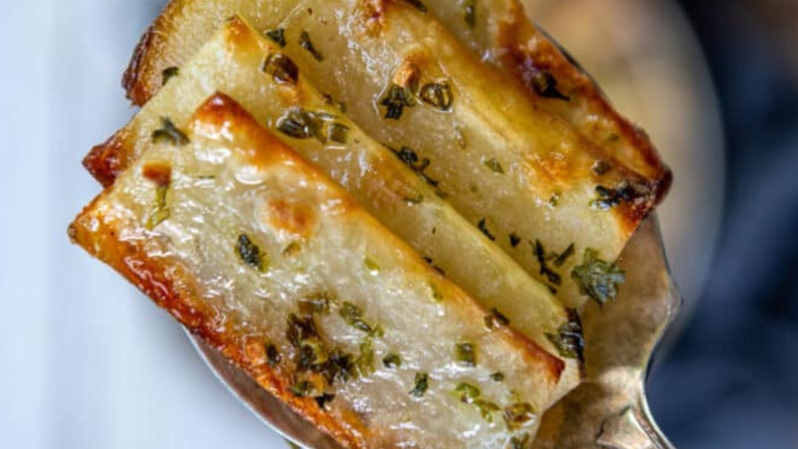 Close-up of cooked potato wedges topped with herbs on a spoon.