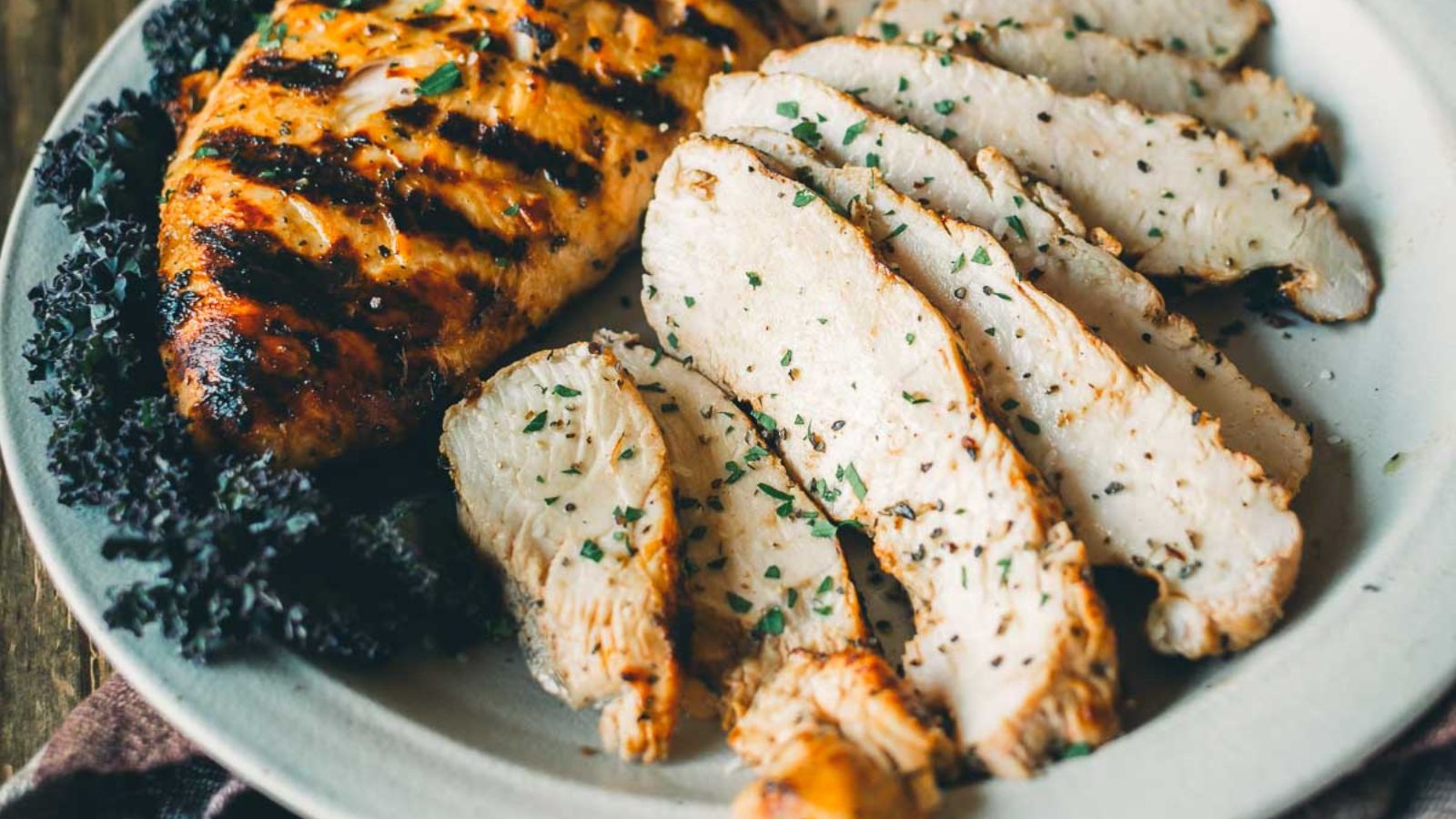 Grilled turkey tenderloin, sliced and garnished with herbs, on a white plate with a side of kale.