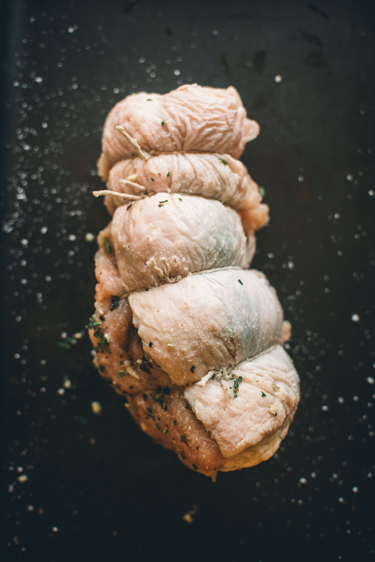 Raw, seasoned turkey breast rolled and tied with string on a dark background.