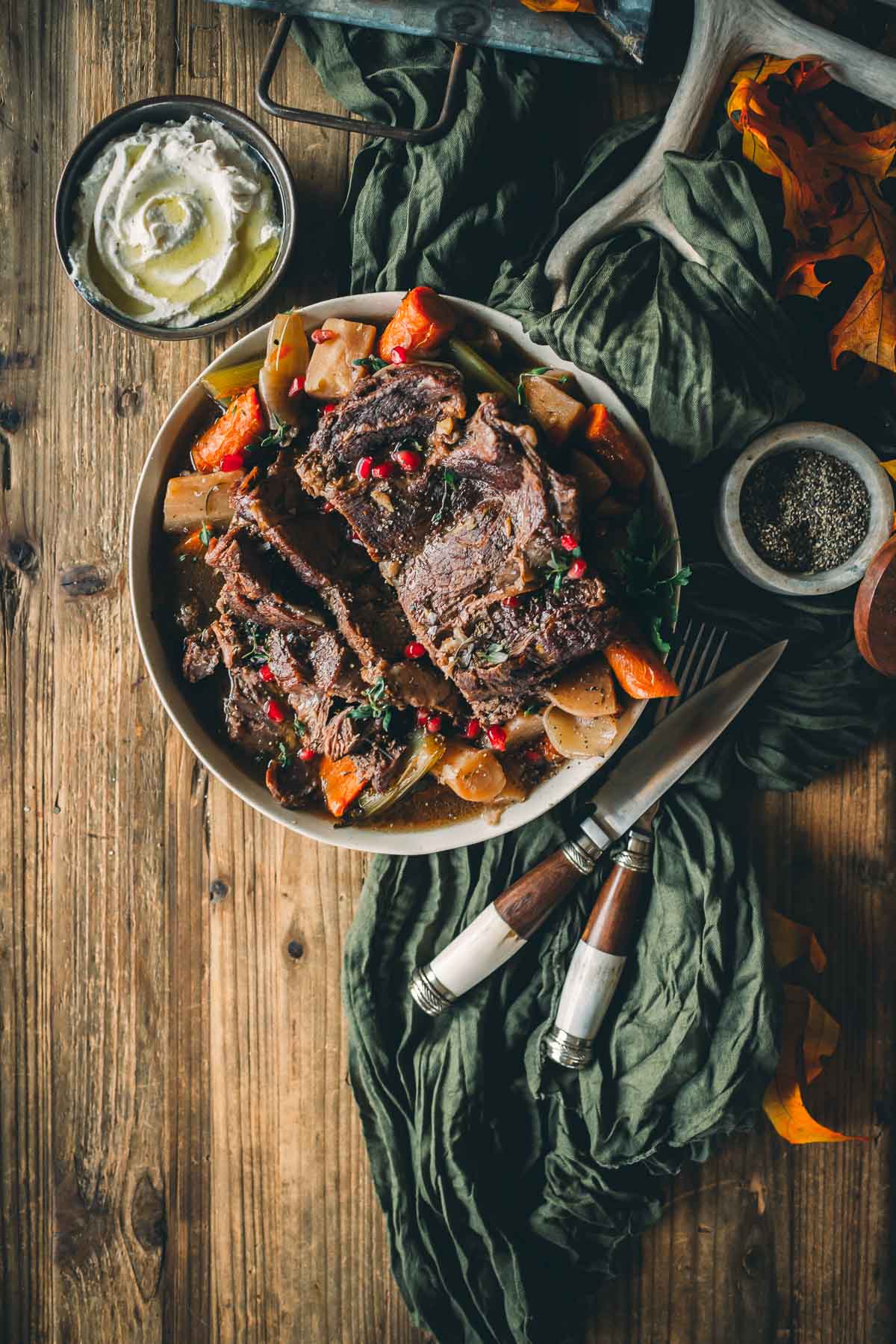 A rustic wooden table with a plate of Instapot pot roast, vegetables, and garnishes.