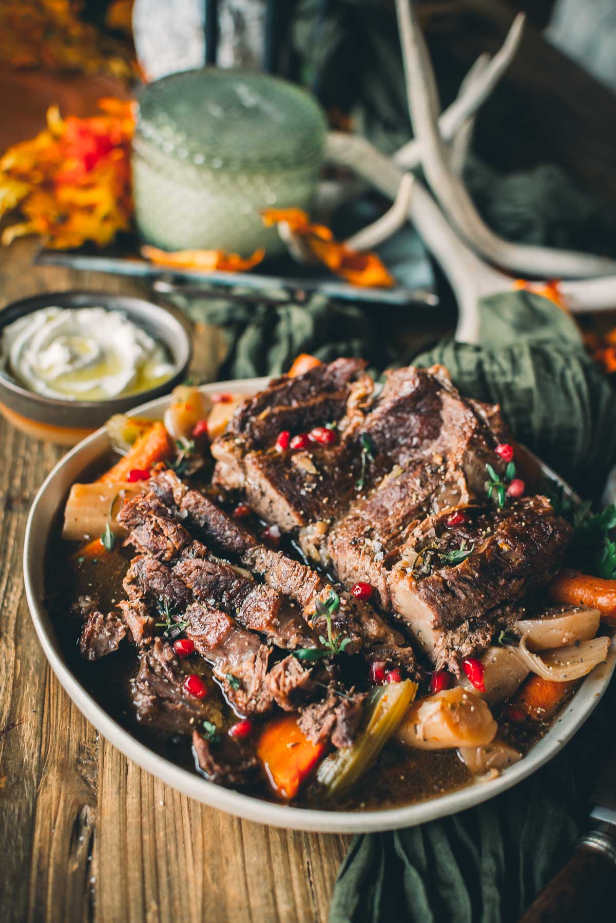 A plate of Instantpot pot roast garnished with herbs and pomegranate seeds, surrounded by vegetables.